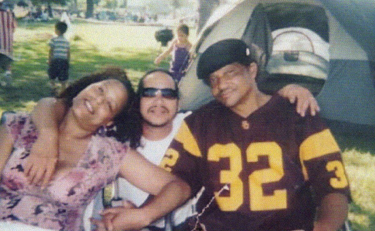Andre Butler, wearing a sports jersey, poses with a man and a woman.