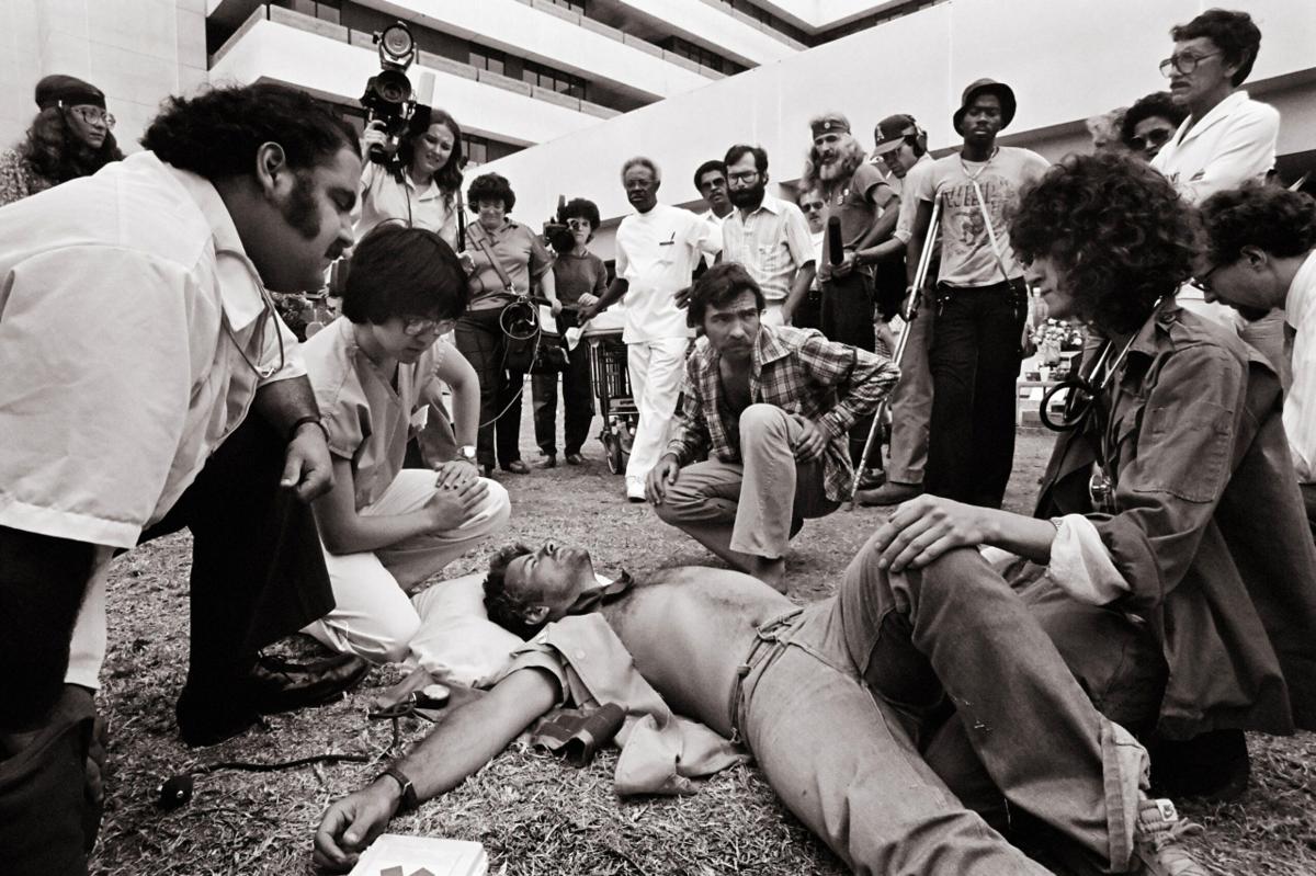 Press and onlookers gather around a collapsed Vietnam veteran at a VA protest, 1981.