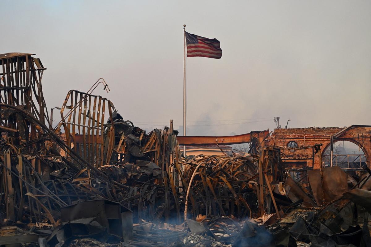 A blackened US flag flies above a charred structure after the passage of the Palisades Fire in Pacific Palisades, California, on January 8, 2025.